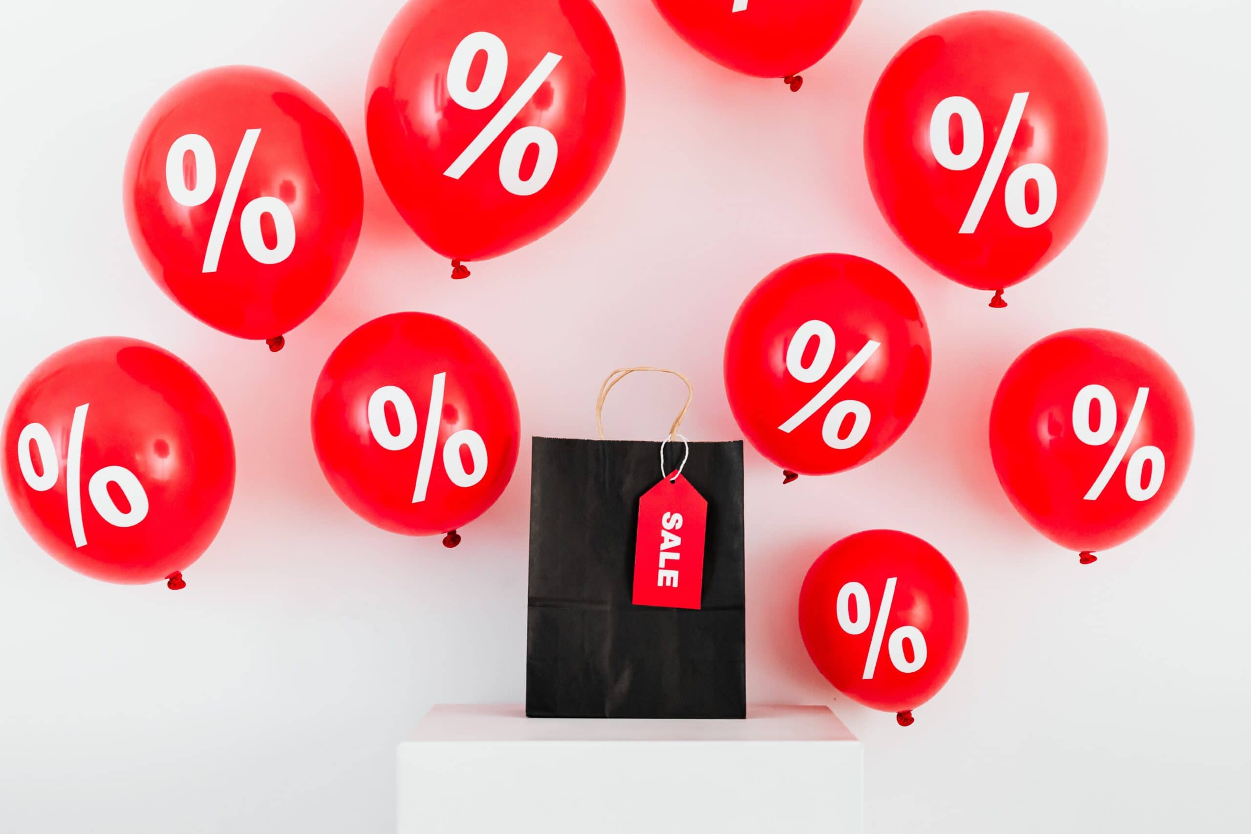Black bag with red sale tag, surrounded by red balloons with white % signs on themthem